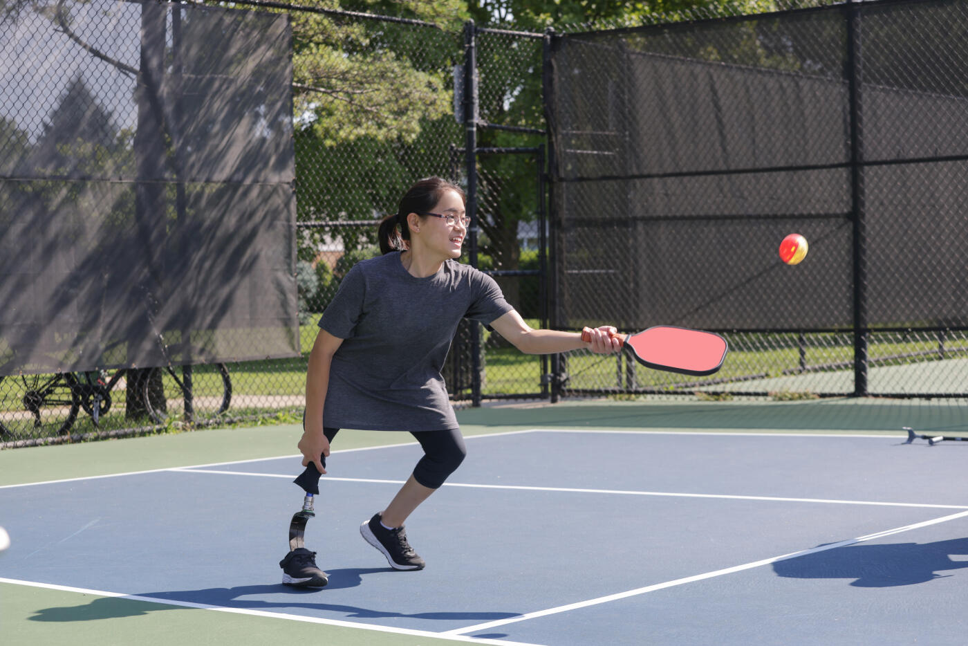 A disabled Chinese teenage girl plays pickleball outside during the summer while wearing casual clothing.