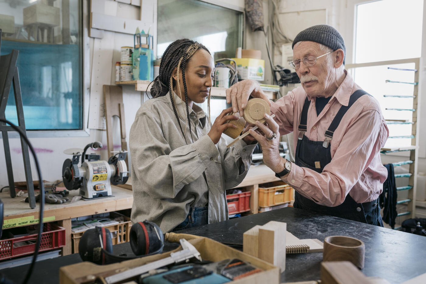 A mature wood workshop owner assisting a student with a project she's working on in his studio.