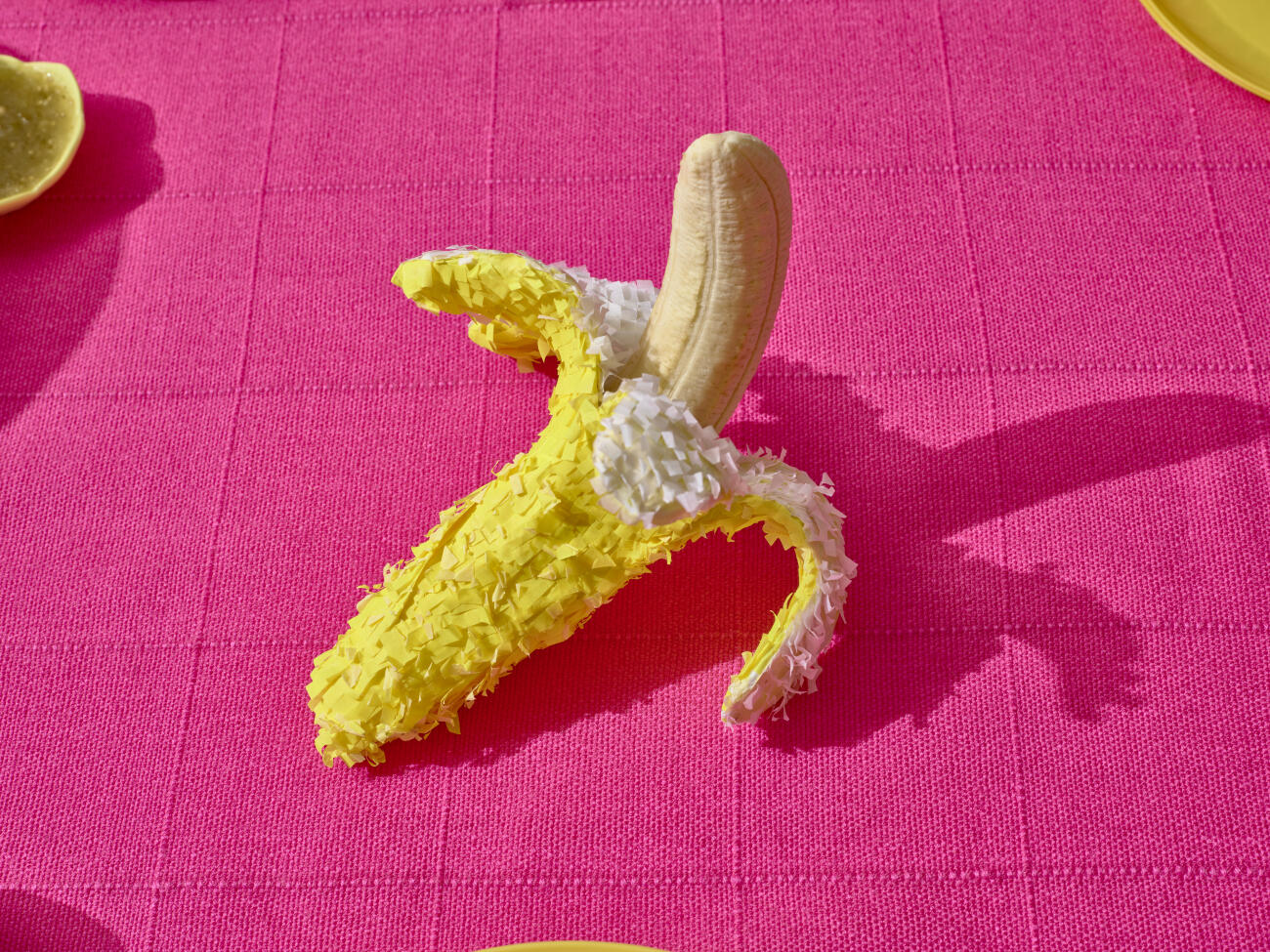 A handcrafted piñata banana shot over a table with a bright light over a mexican pink bright tablecloth.