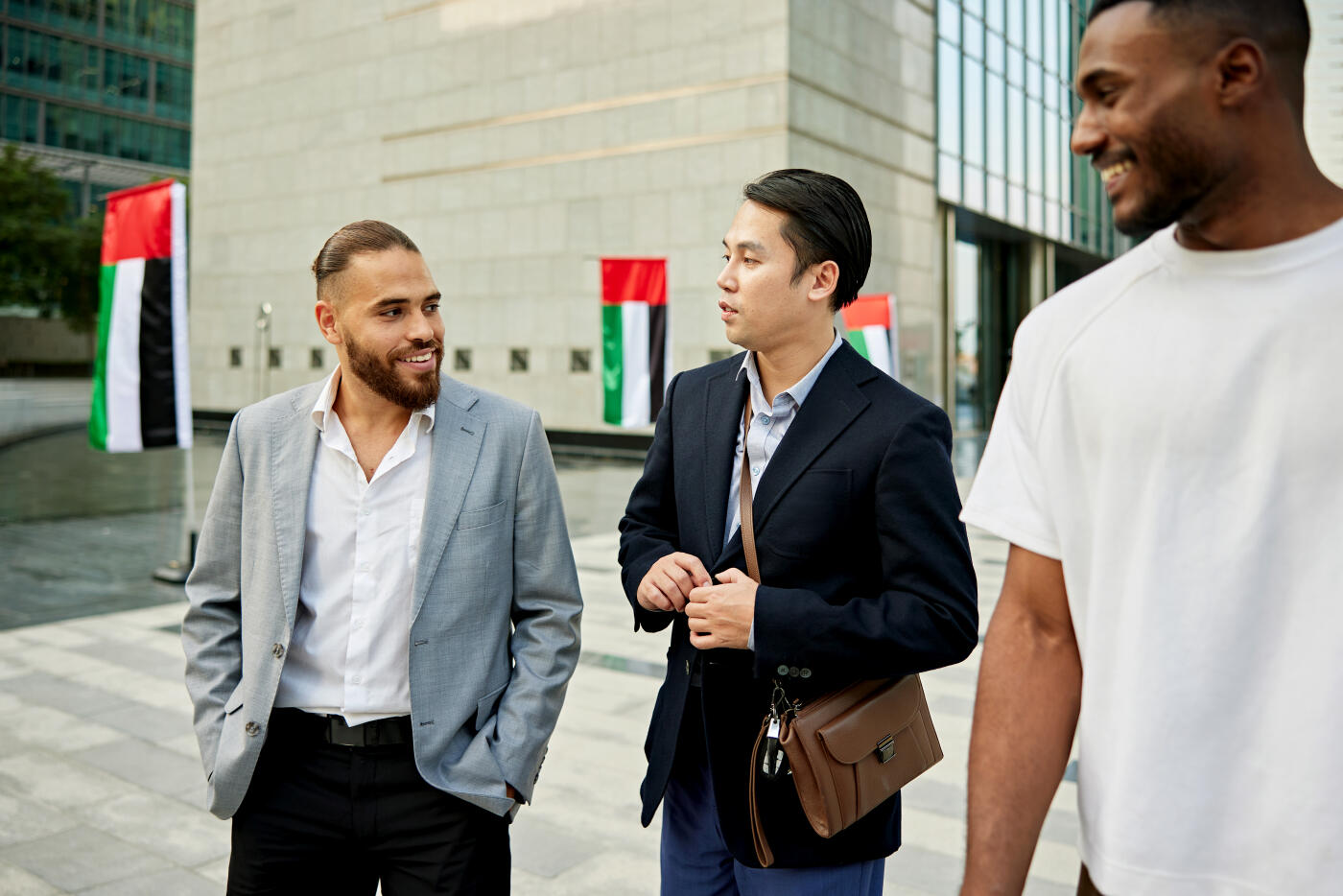 Casually dressed men in 20s and 30s taking a break, smiling and interacting, UAE flags in background.