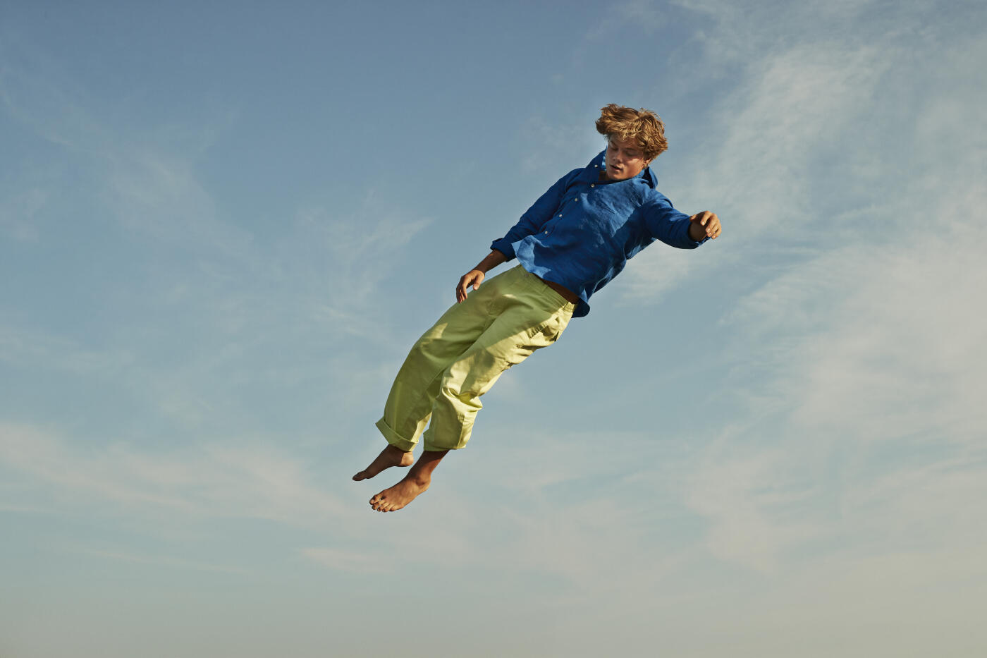Low angle view of young man levitating high in mid-air against blue sky