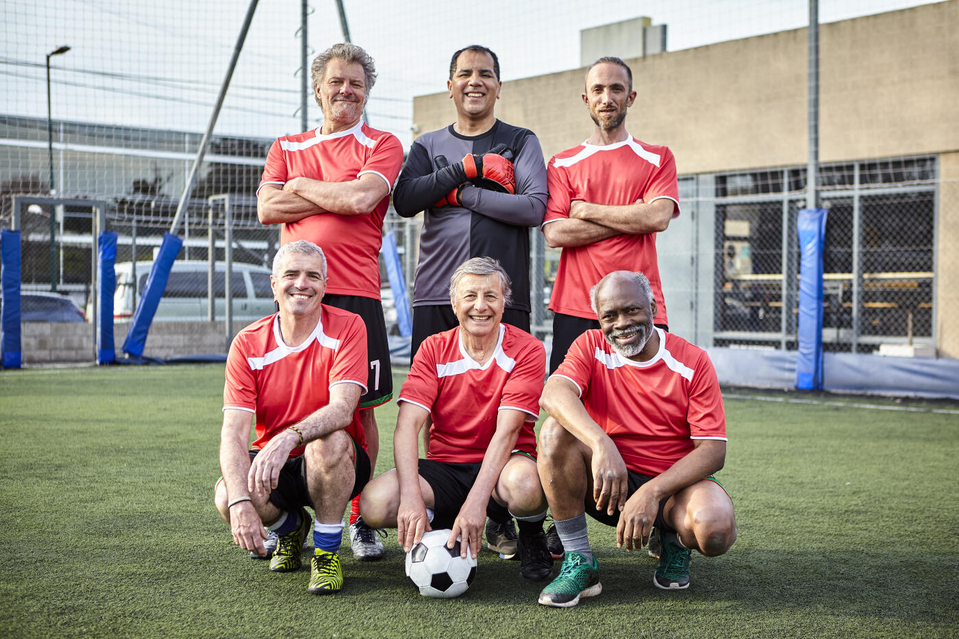 Full body portrait of amateur football team of middle-aged male players posing together in playing field before match
