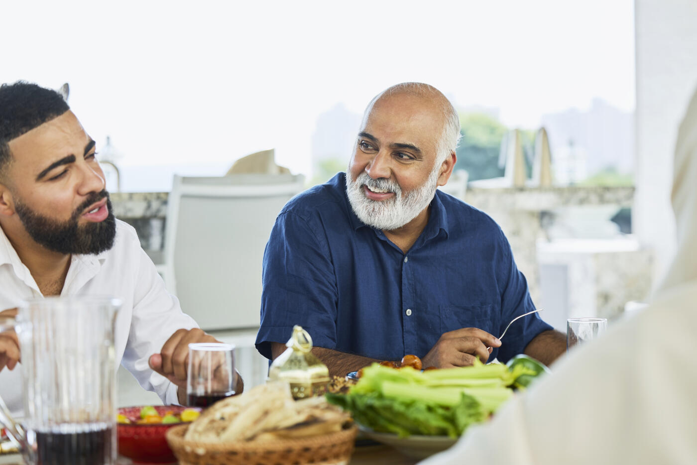 Smiling senior man sitting next to son while having lunch. Men talking during meal time. They are wearing casuals.