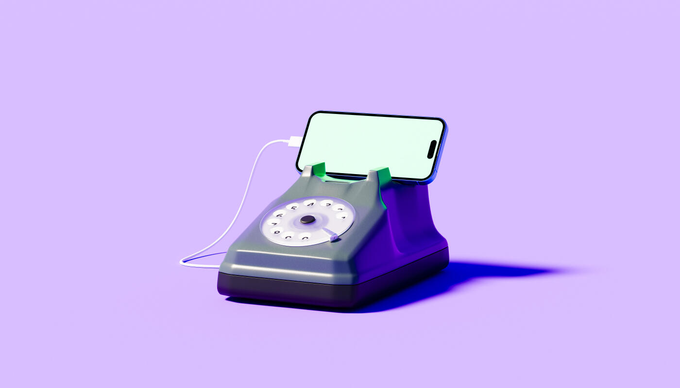 Conceptual image of a vintage gray and orange rotary dial telephone creatively adapted as a stand and charging cradle for a contemporary smartphone with illuminated blank screen connected by white cable against a soft peach studio background illustrating form versus function between analog and digital eras.