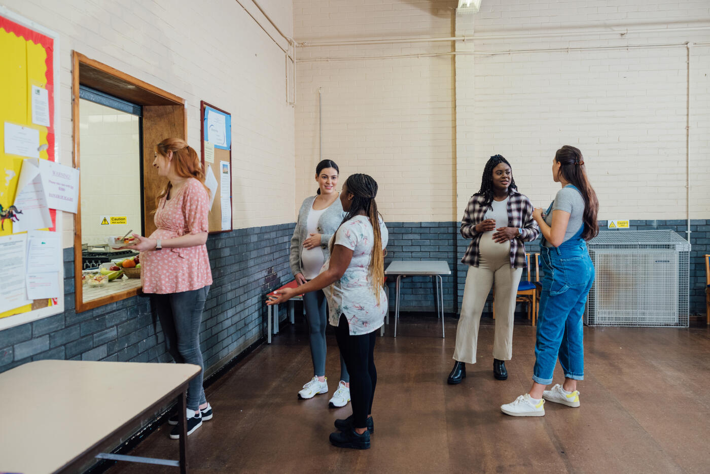 A wide angle view of a group of five pregnant women all in their third trimester of their pregnancy chatting and sharing stories before they take part in a antenatal fitness class in a community centre in the North East of England.