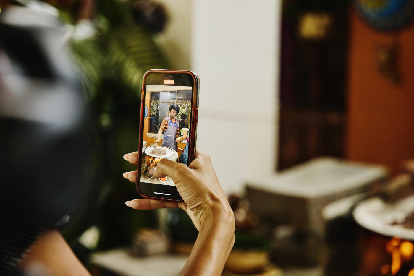 Medium close-up of hand using phone to photograph man roasting cocoa beans on comal grill during experiential cooking class while on vacation