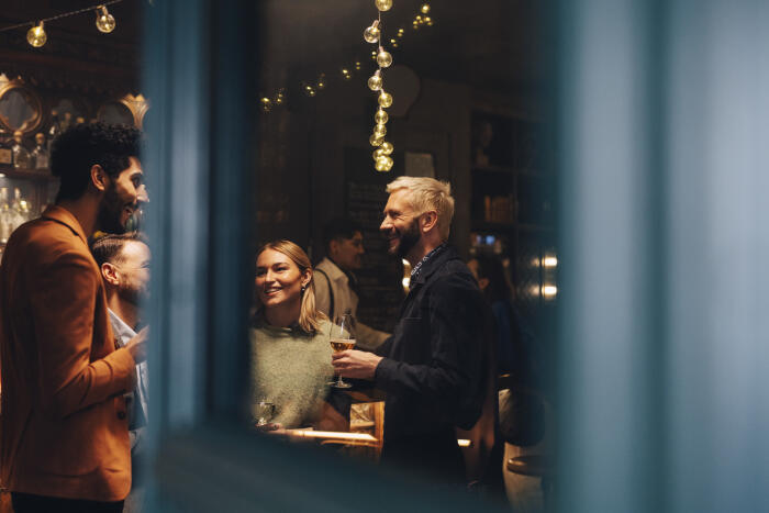 Smiling male and female friends talking to each other in club seen through glass