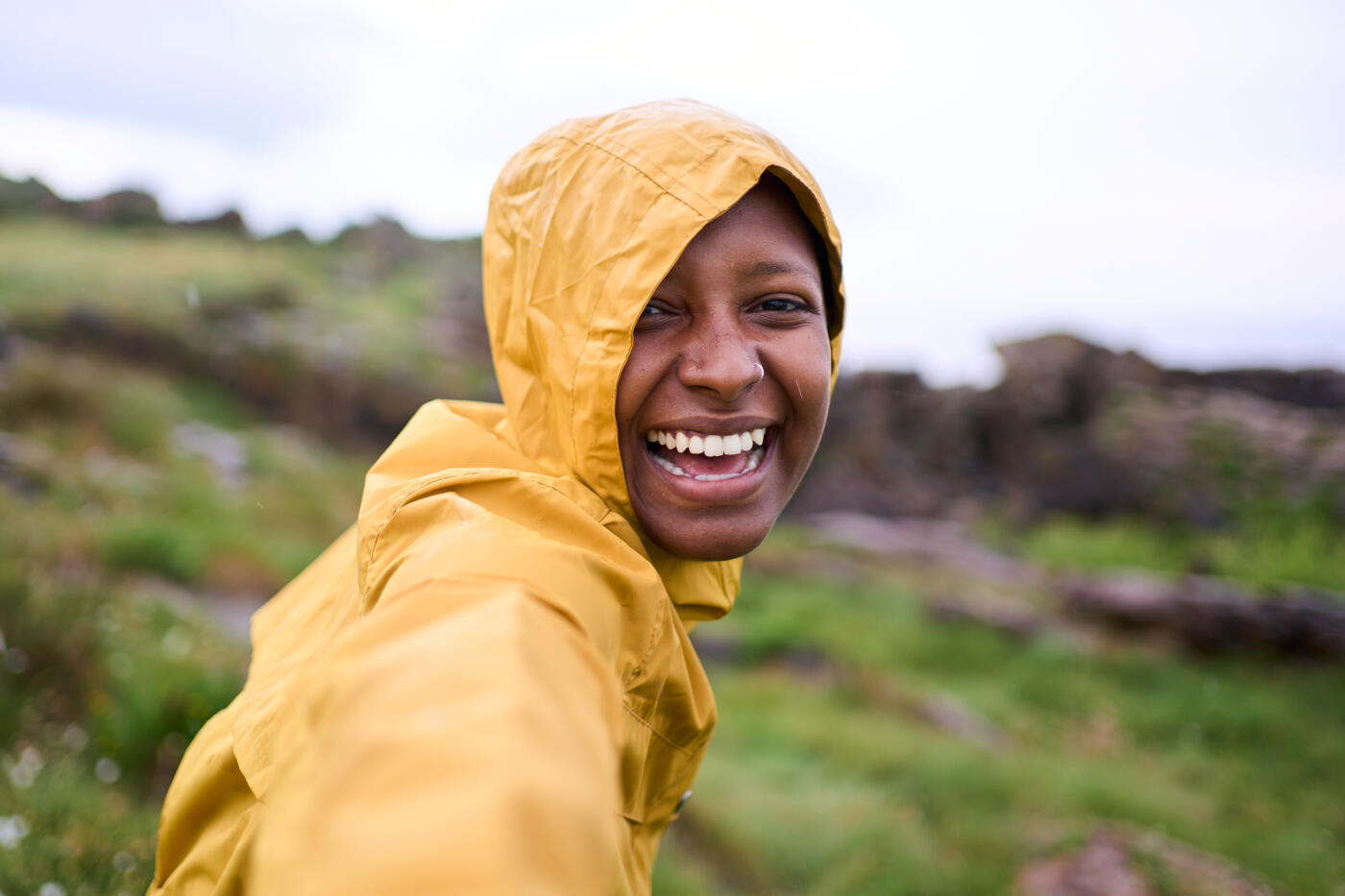 Happy woman looking at camera with big smile while being outdoors under the rain wearing a yellow raincoat. Close up