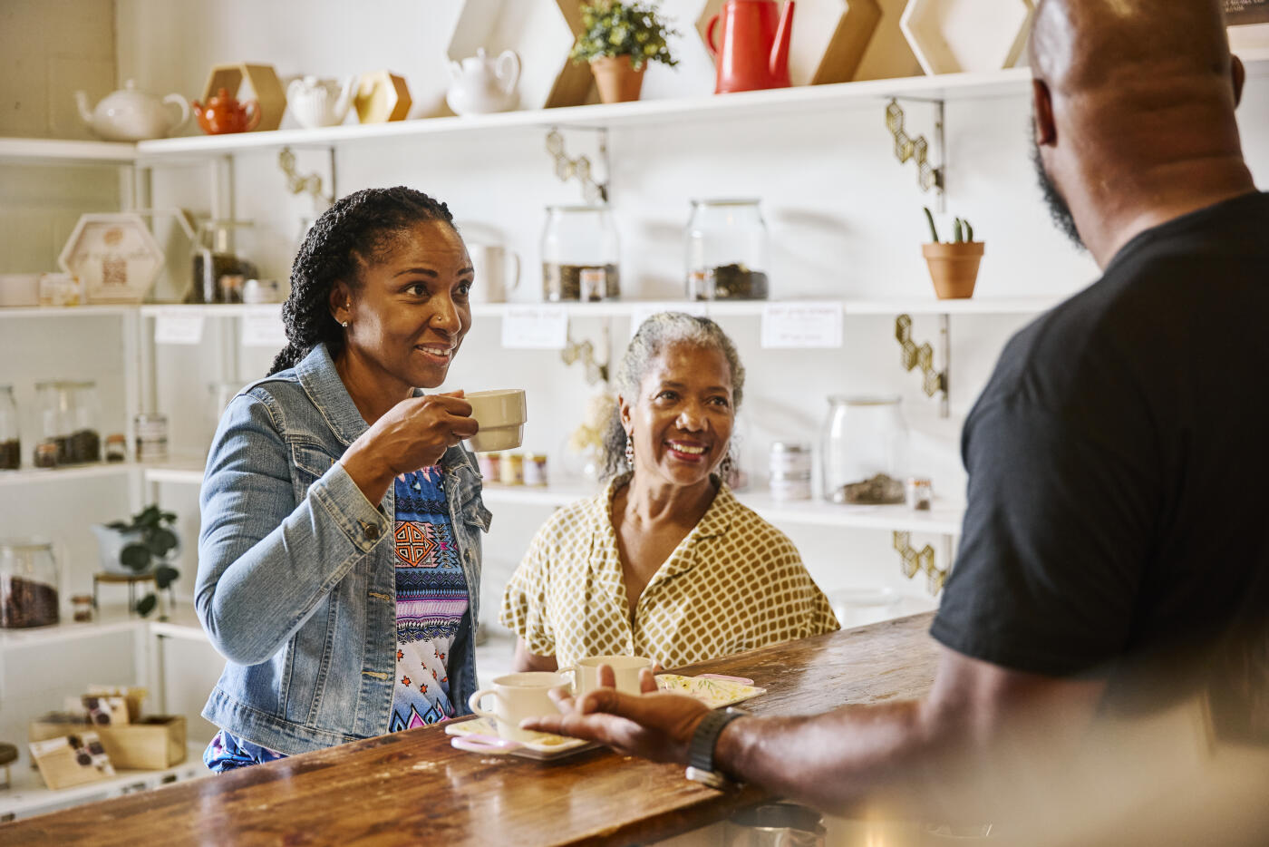 Smiling woman attentively listening to a male shop owner describe the diverse flavors of hot teas during a tasting session at a specialty tea shop.