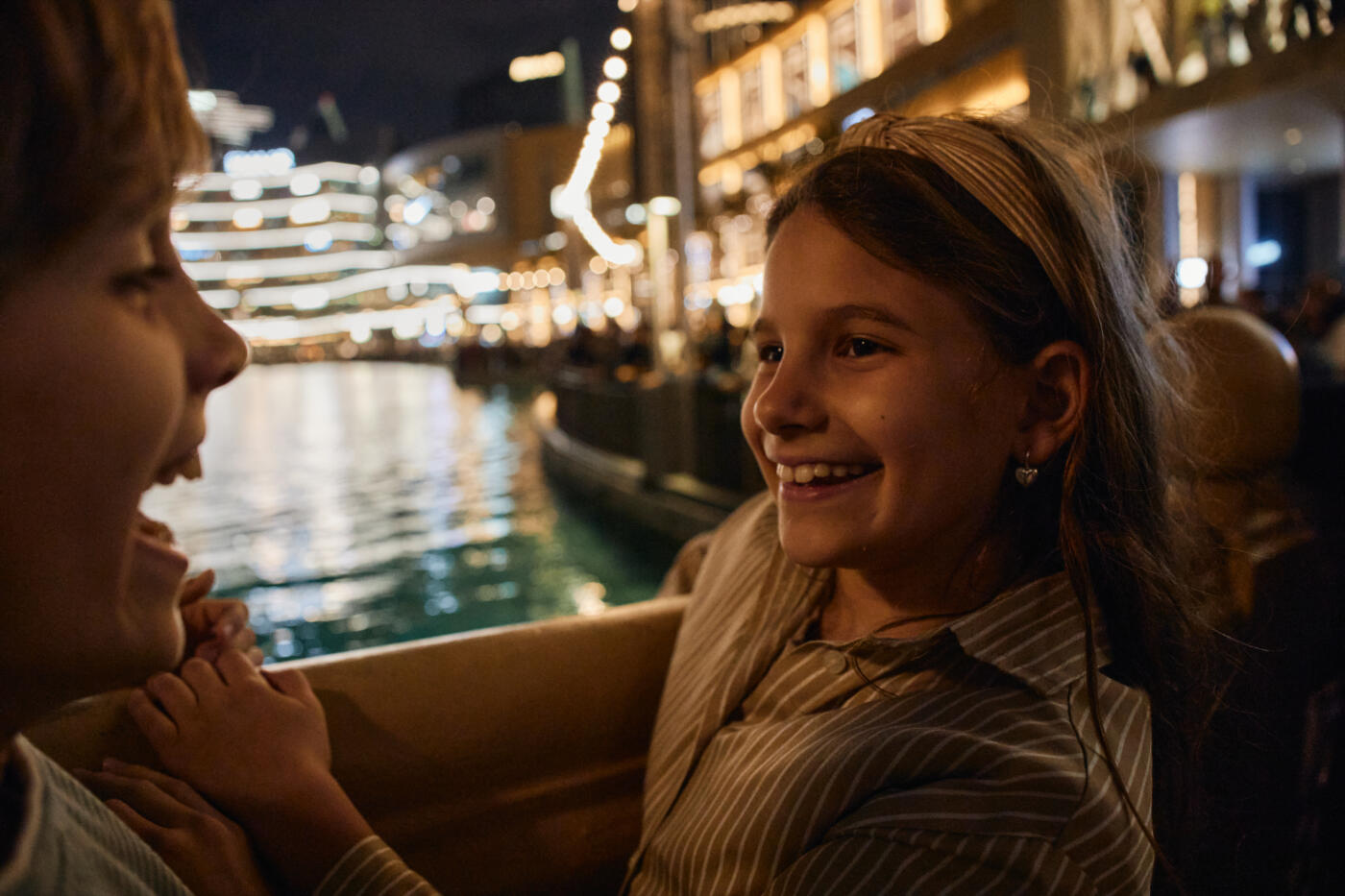 Children laughing and smiling while traveling on a boat at night with city lights
