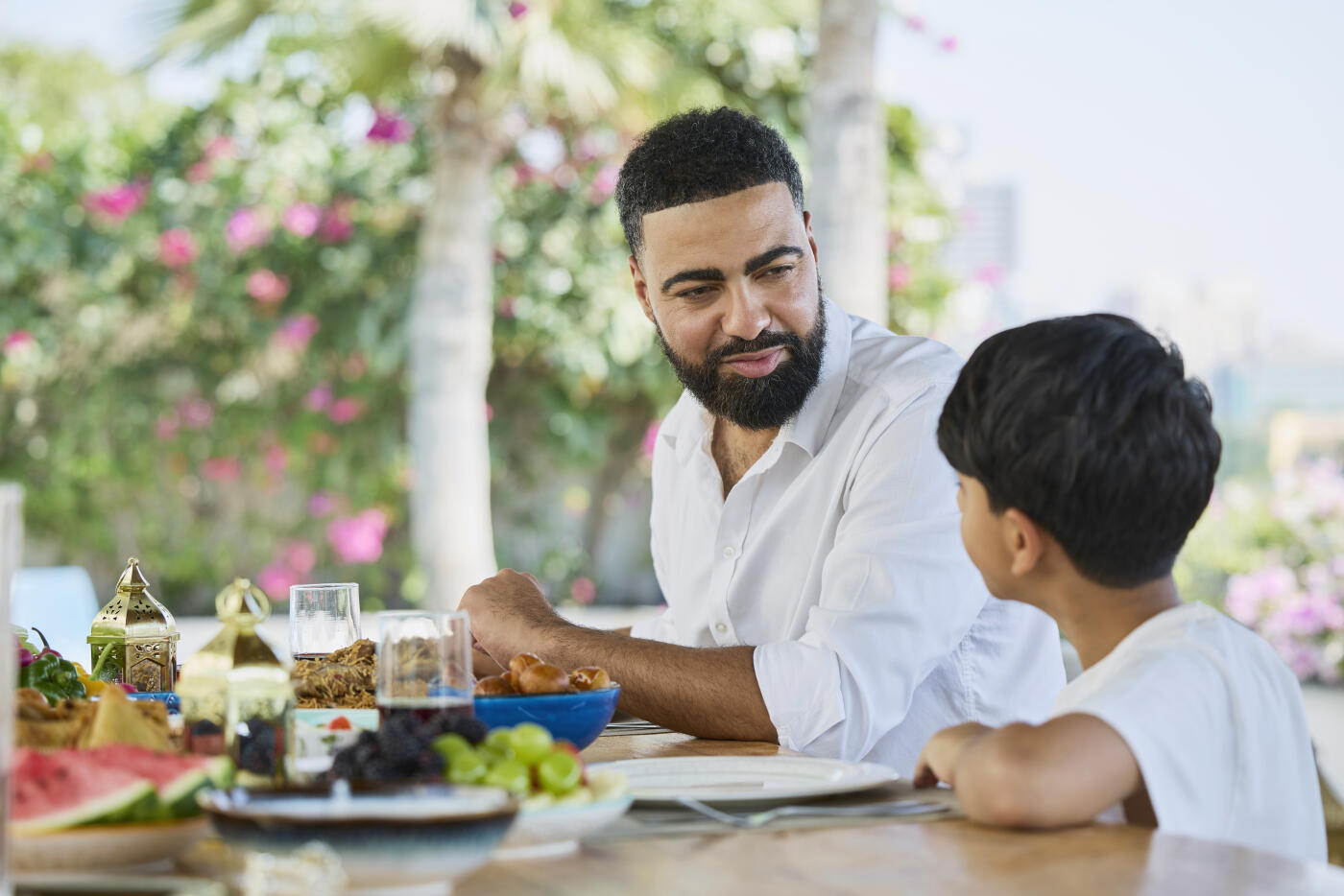 Father having lunch with son sitting at dining table. Man is talking with boy. He is wearing shirt.