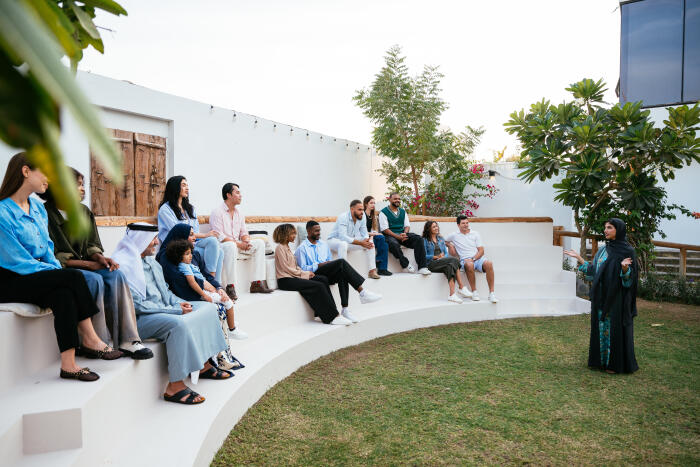 Diverse group of people attending an outdoor seminar or presentation on a modern, stylish outdoor patio with greenery and contemporary architecture