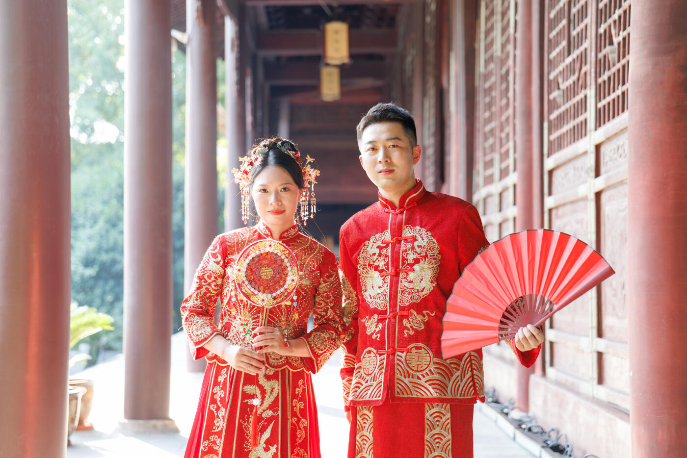 A Chinese newlywed couple in their 30s on their wedding day, wearing Hanfu costumes, walking in a traditional Chinese street, holding traditional Chinese fans, looking at the camera