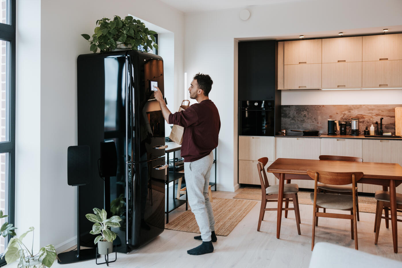 Man, holding a shopping bag, interacts with his smart fridge, highlighting the seamless connection between technology and daily life