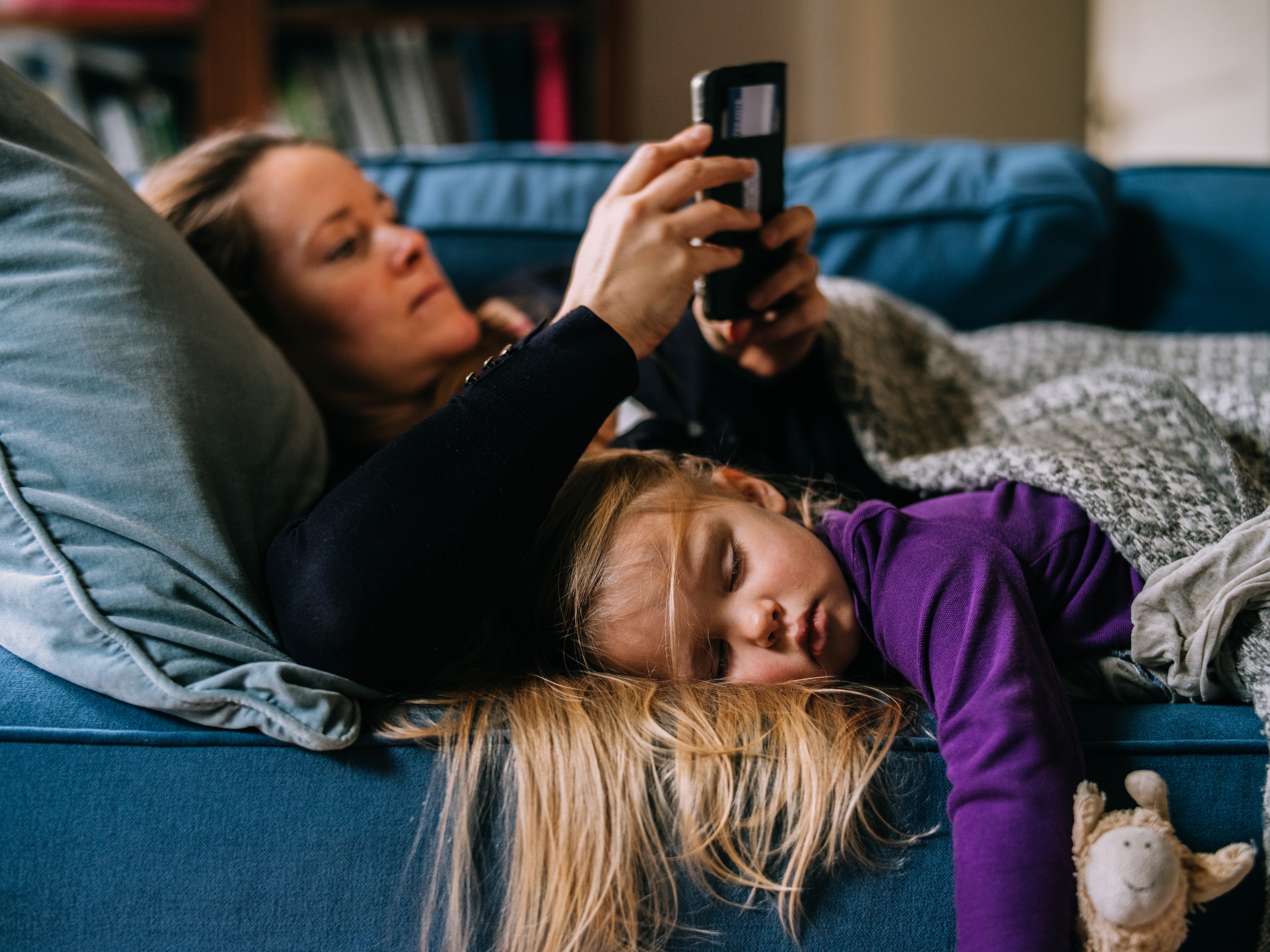 Vrouw die haar mobiele telefoon gebruikt terwijl haar dochter op de bank slaapt.