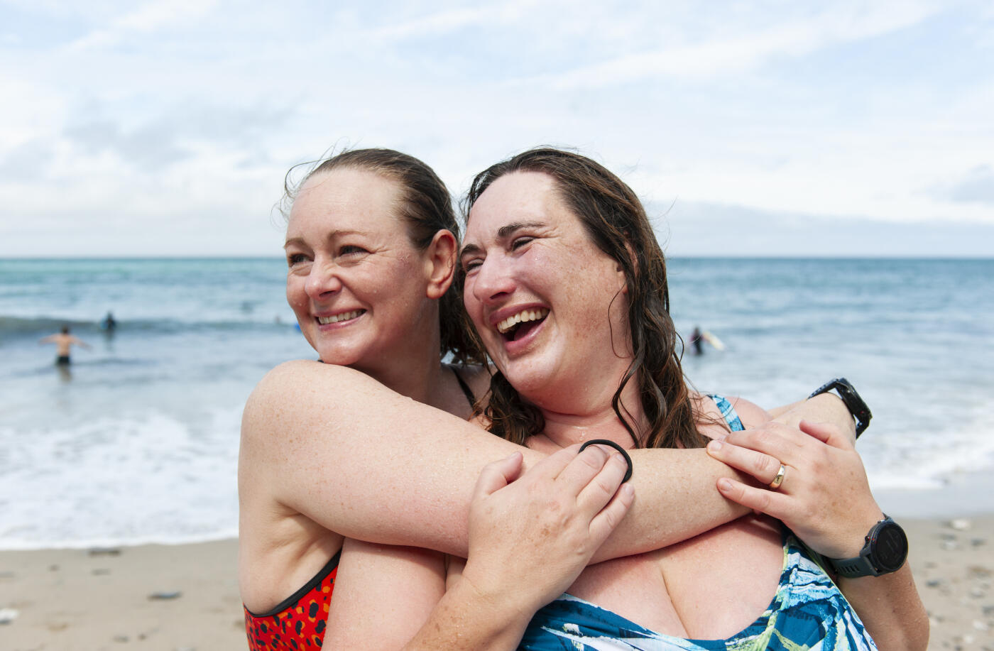 UK, Cornwall, female swimmer embracing and laughing on a beach after swimming in the sea