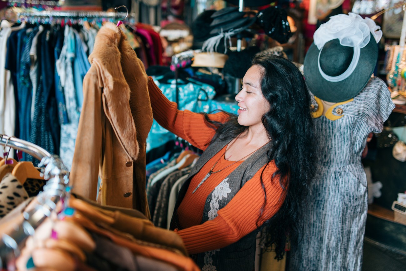 An Indigenous Alaskan woman shops in a fun fashion thrift shop, trying on clothing and hats and putting together outfits.  Shot in Anchorage, Alaska.