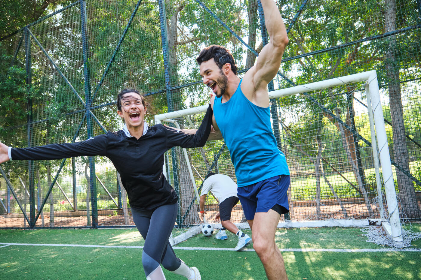 Woman enjoying with male friend after scoring goal. Sportspeople are jumping on turf. They are celebrating with hand raised.