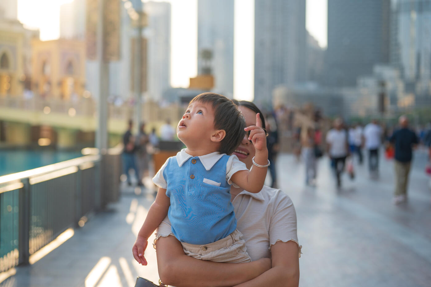 A mother lifts her child joyfully as they gaze at something captivating in the bustling urban landscape, capturing a moment of wonder and connection in their familial bond amidst the city backdrop.