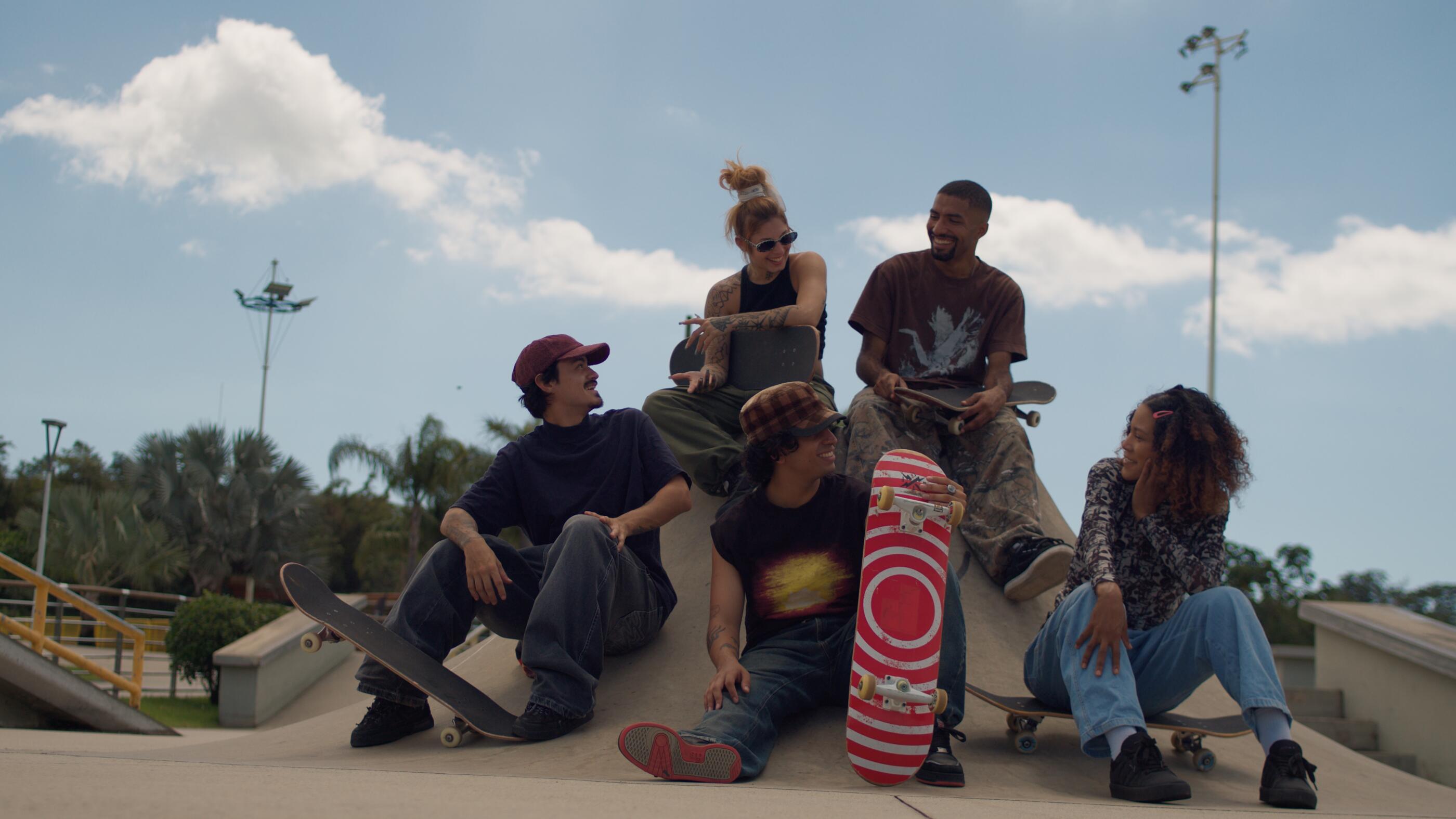 Group of young skateboarders sitting and standing together at a skatepark on a sunny day.