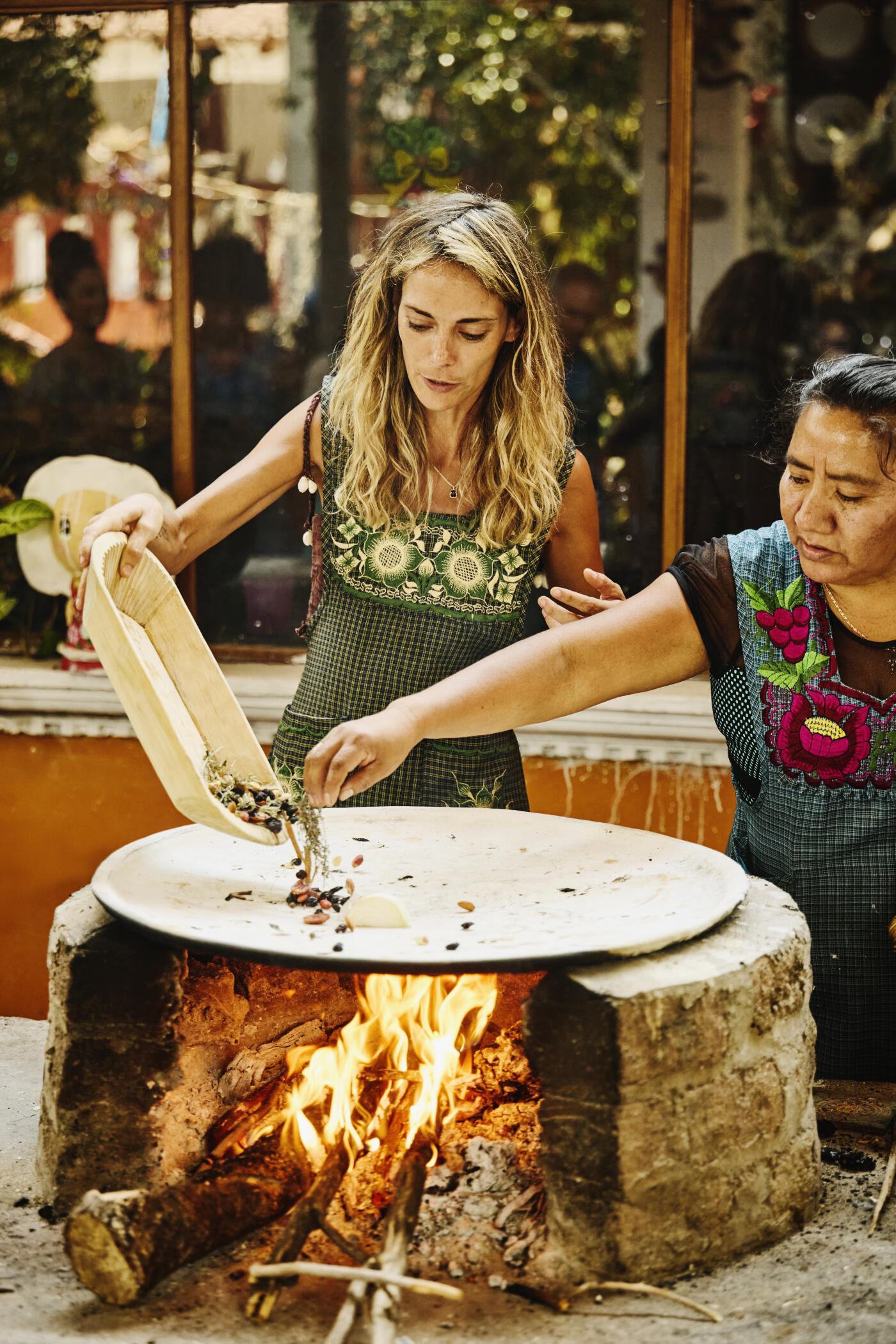 Medium shot of female student and teacher cooking herbs and nuts on wood-fired comal grill during traditional Mexican cooking class