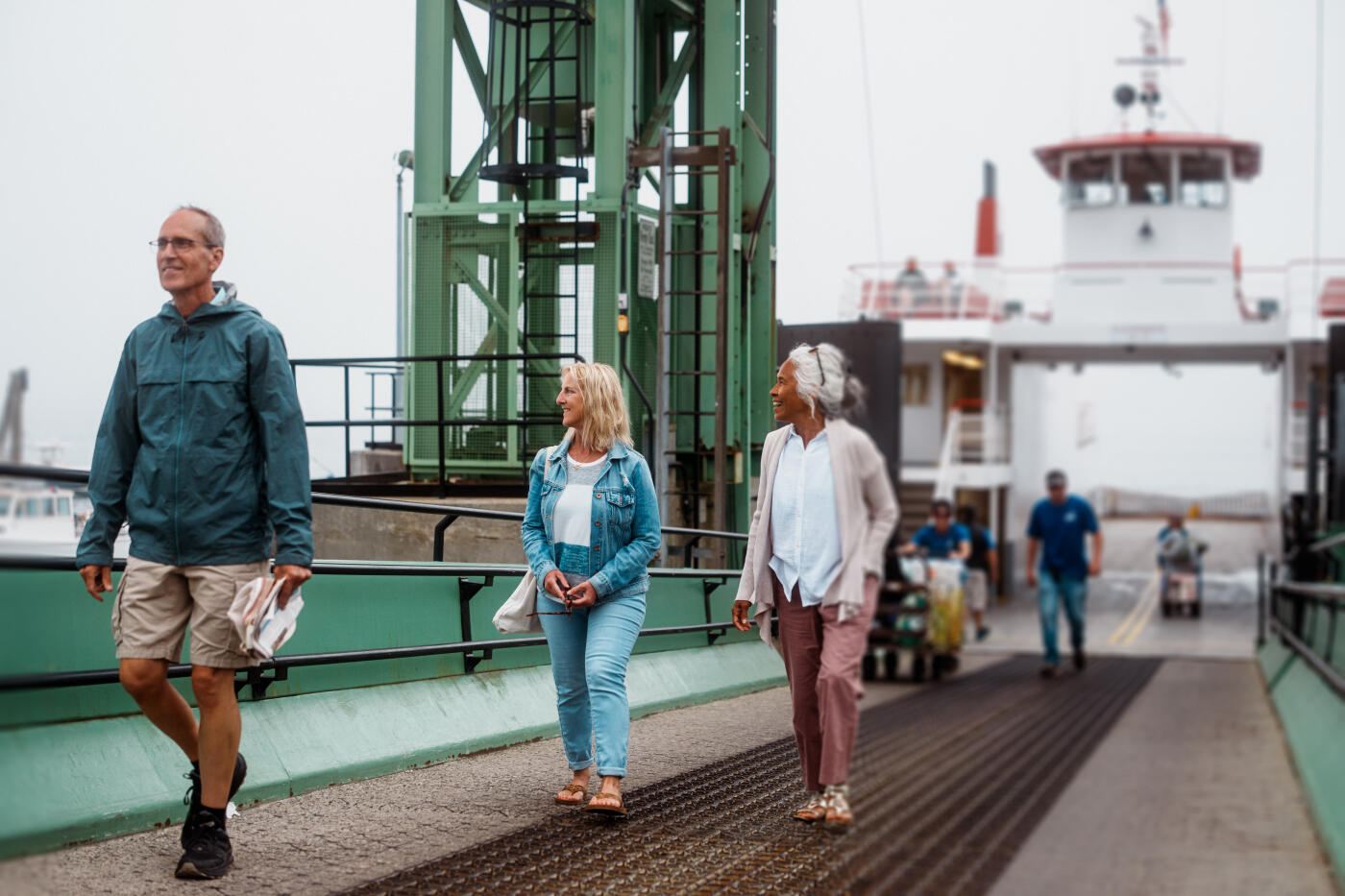 Three senior friends walk off the ferry ramp onto Peaks Island, Maine, smiling as they begin their visit.