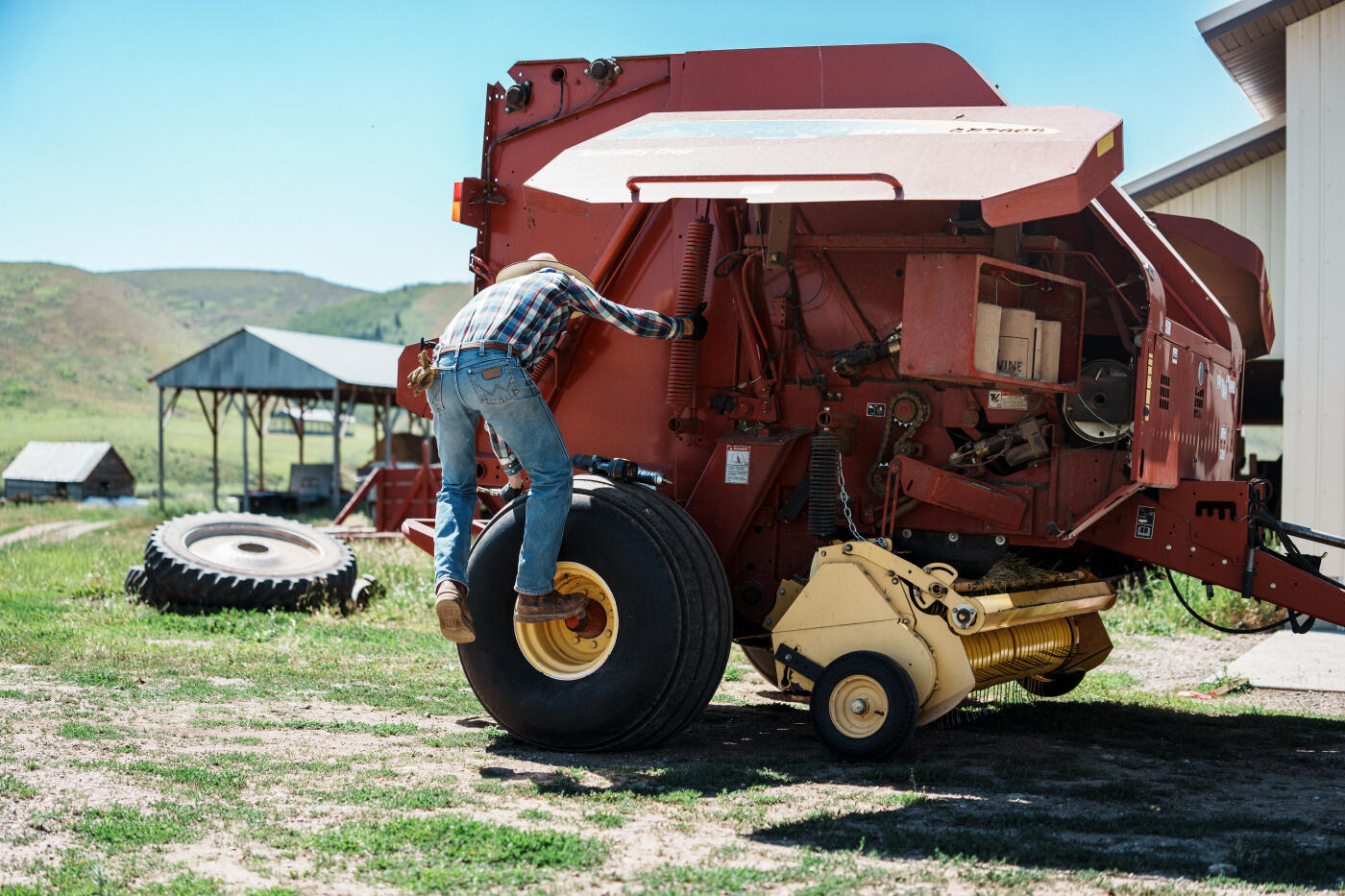 A rancher maintains a large hay baler beside a barn on his Wyoming ranch during summer hay season.