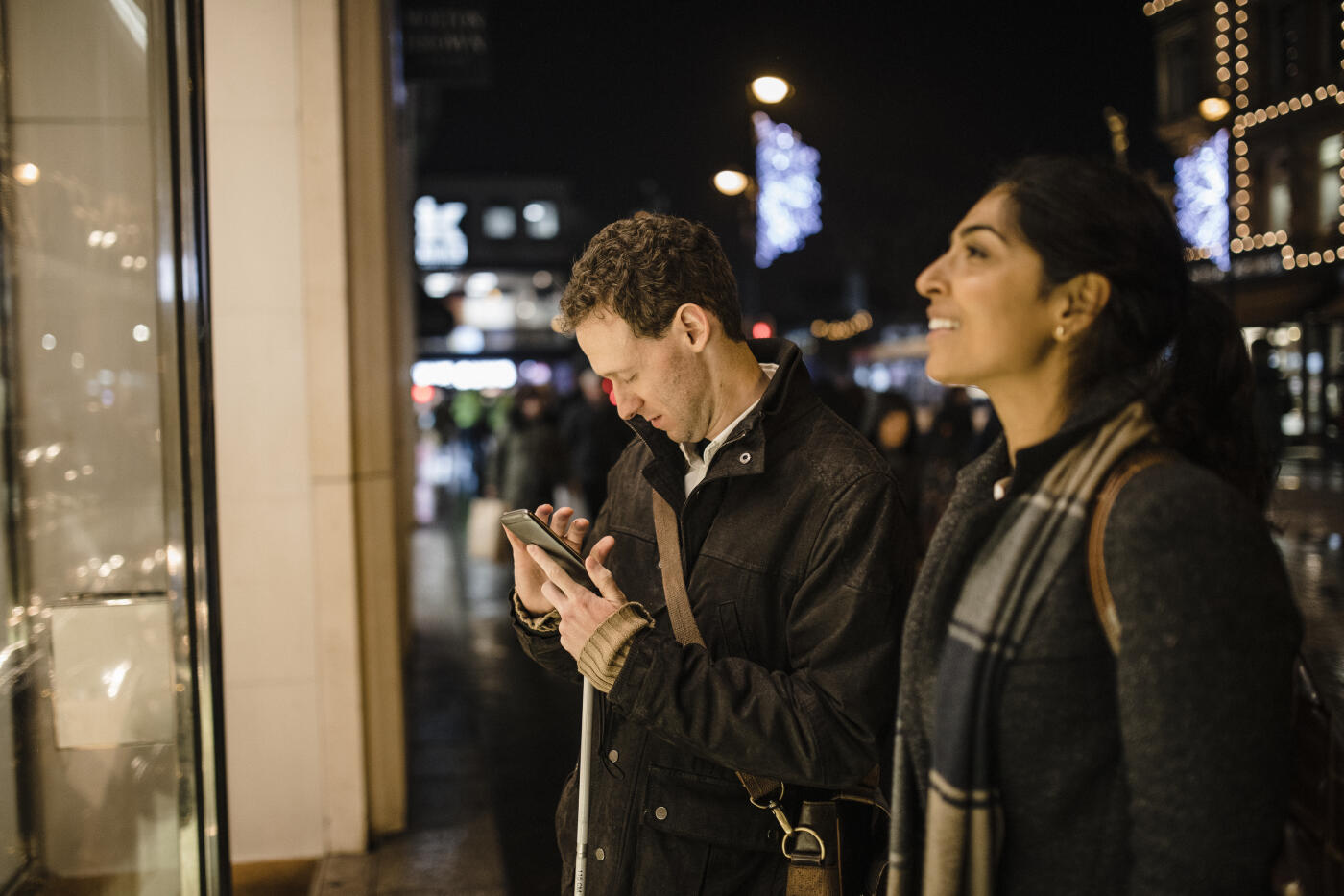 Visually impaired man using his mobile phone to assist him while out shopping with his female friend. Its a cold winter evening in the city centre.