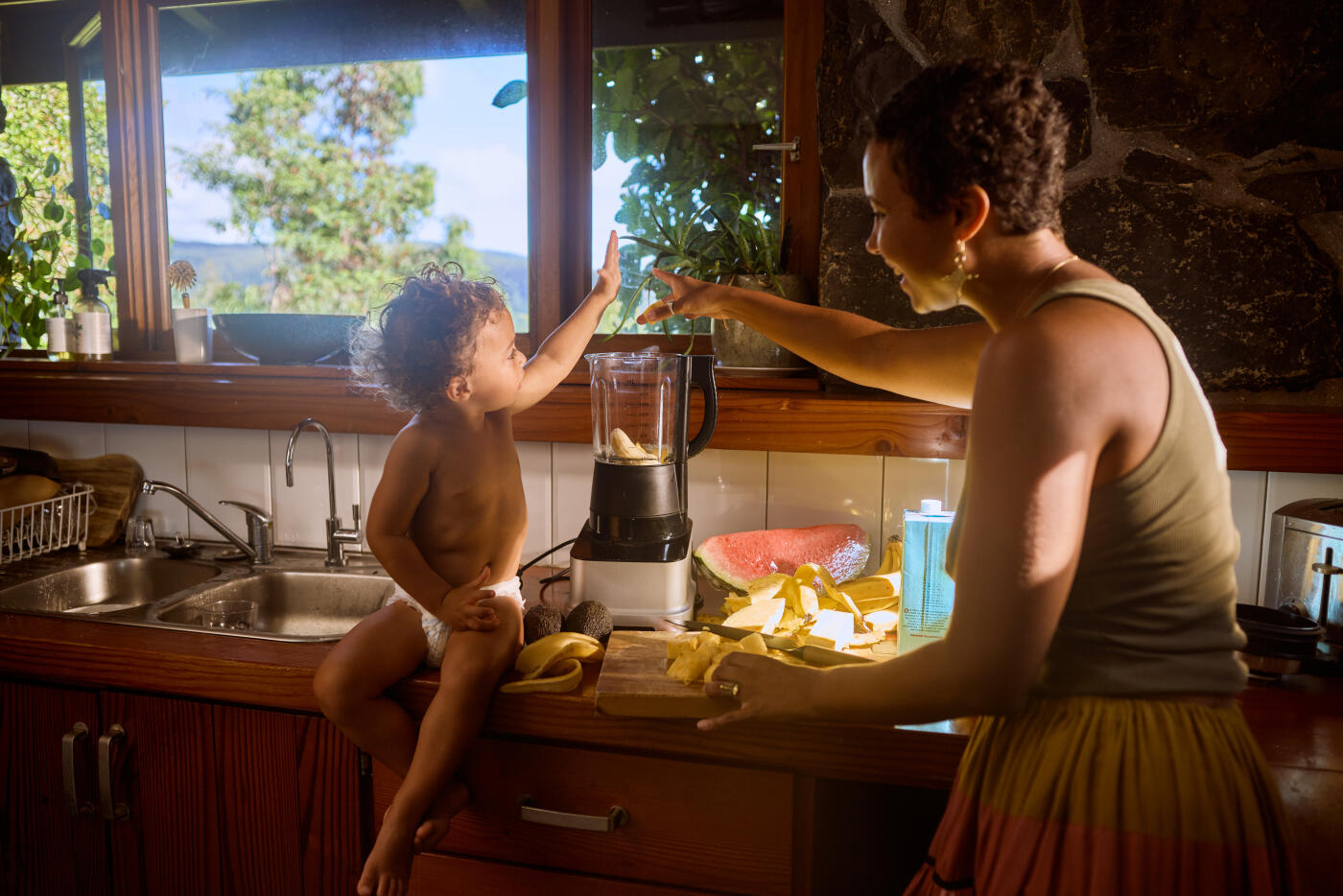 Mother and her young child are making a smoothie together in their rustic kitchen, enjoying the scenic mountain view from the window