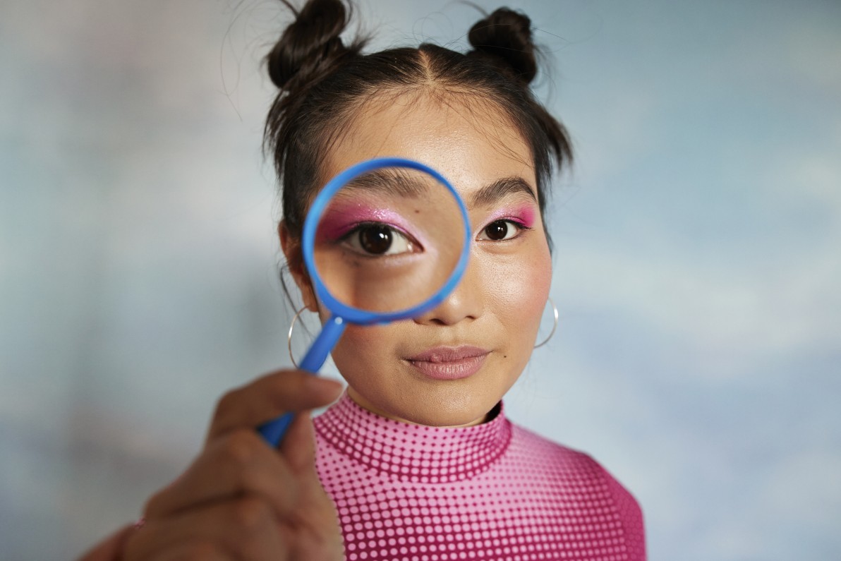 Teenage girl with magnifying glass against colored background