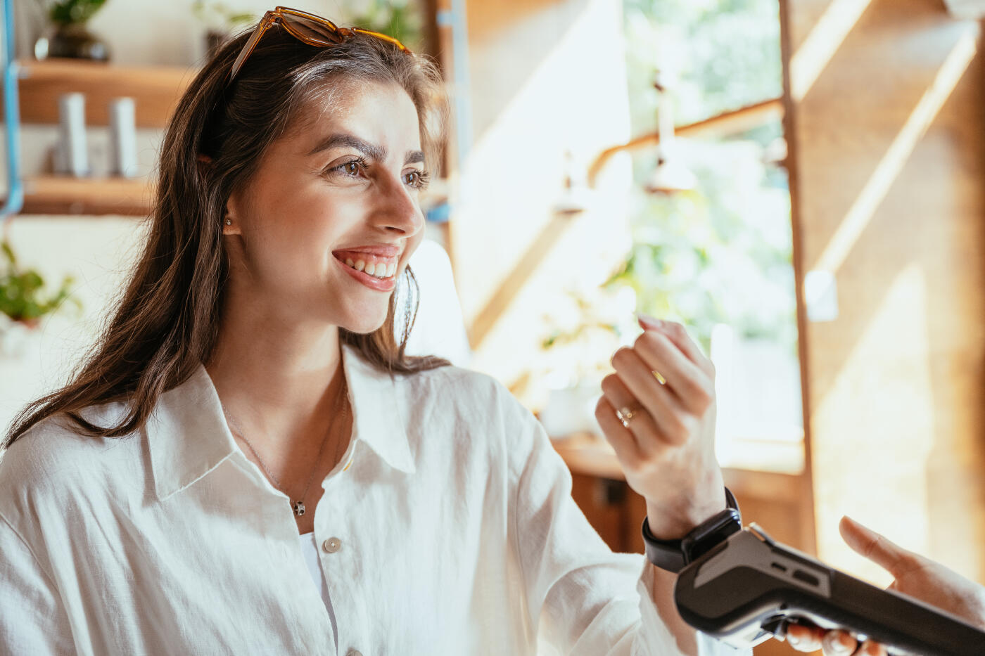 Female barista with hijab working in modern cafe, preparing coffee and serving customer who is paying with smart watch