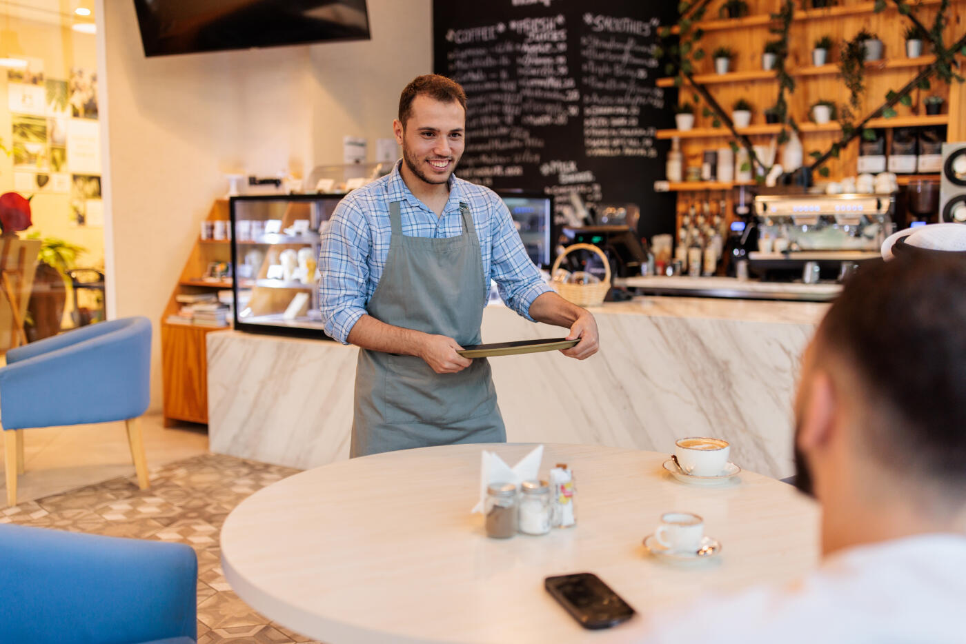 Male waiter speaking with two men seated together in a trendy coffee shop in Dubai.