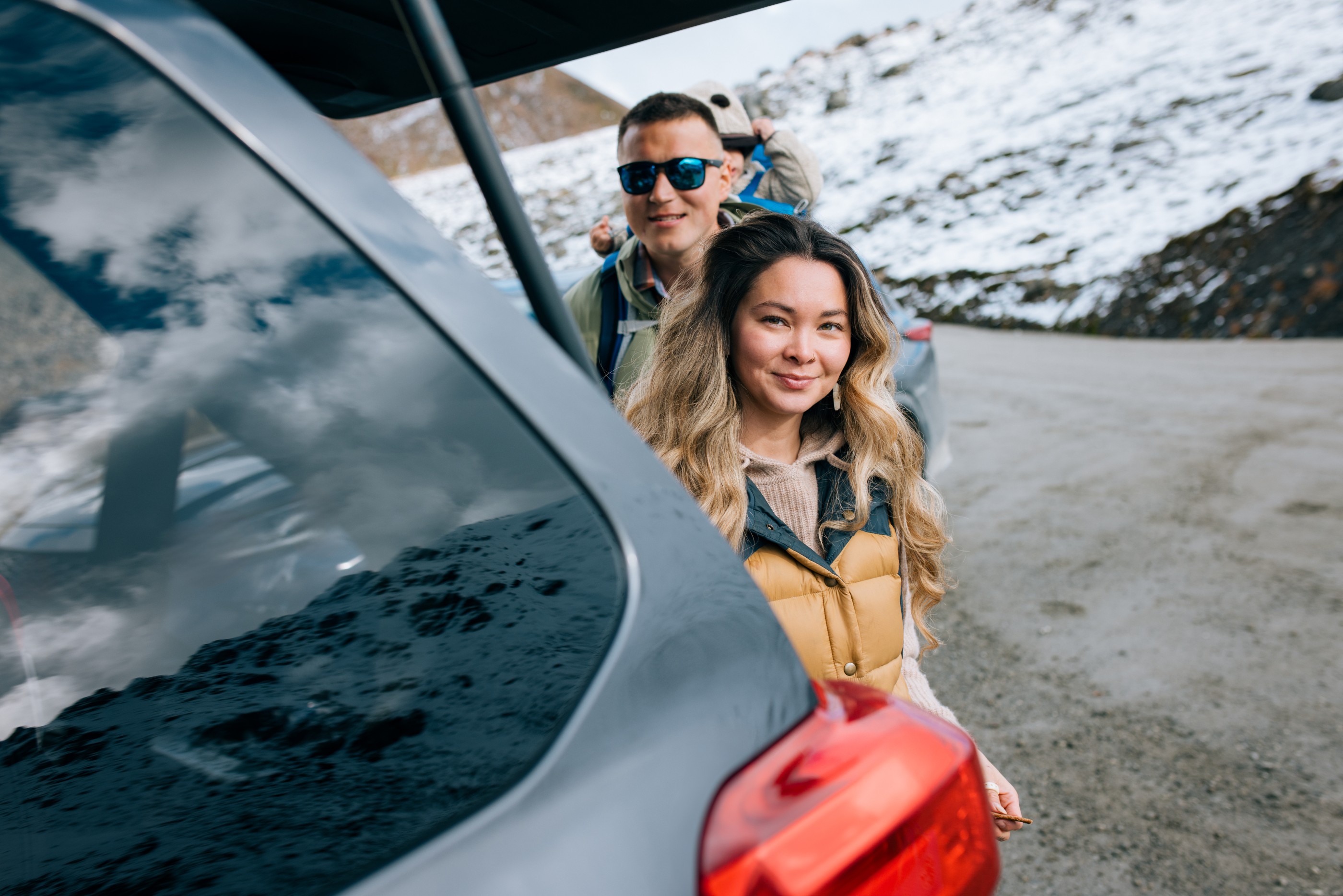 A cute young Indigenous North American family getting ready to explore in the mountains of Alaska with their young child.  They finish loading their gear from their car.  Shot in Hatcher Pass, snow on the ground and mountains surrounding.
