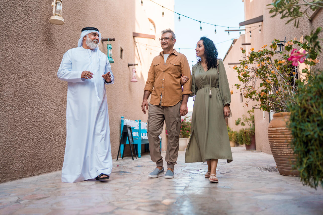 Local Tour Guide In Traditional Dress Leading Couple Through Historic Dubai Alleyway