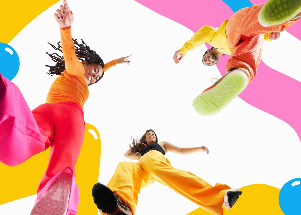 full length studio shot of three people looking down at camera smiling and dancing against colourful background