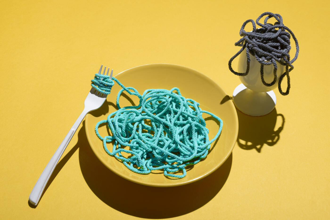 Bowl of bright turquoise yarn/wool pretending to be noodles in yellow bowl and a white glass with black yarn/wool .Studio shot