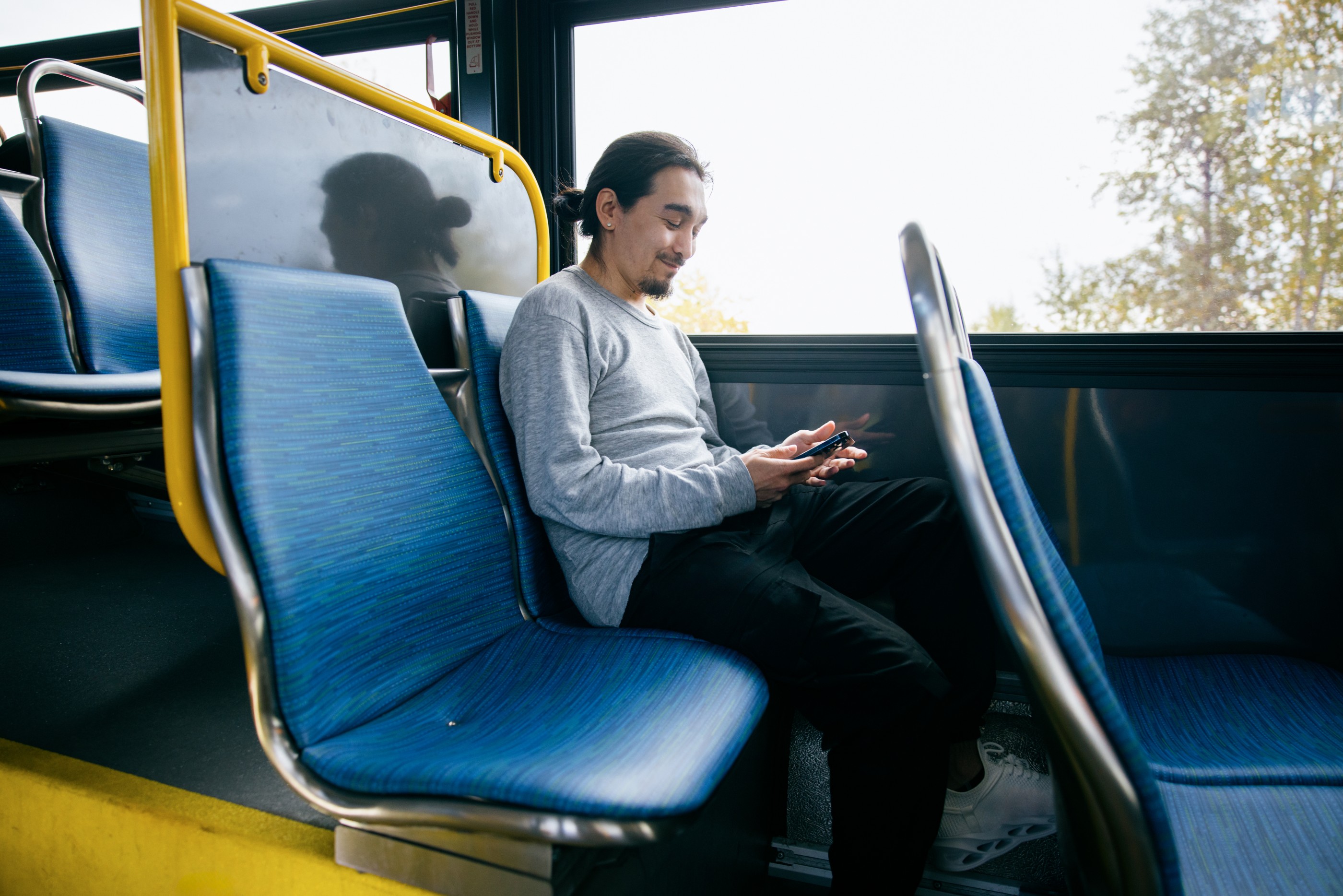 An Indigenous Alaskan man (Yupik tribe) takes the bus in the city of Anchorage, Alaska, USA.  He uses his smartphone to pass the time.