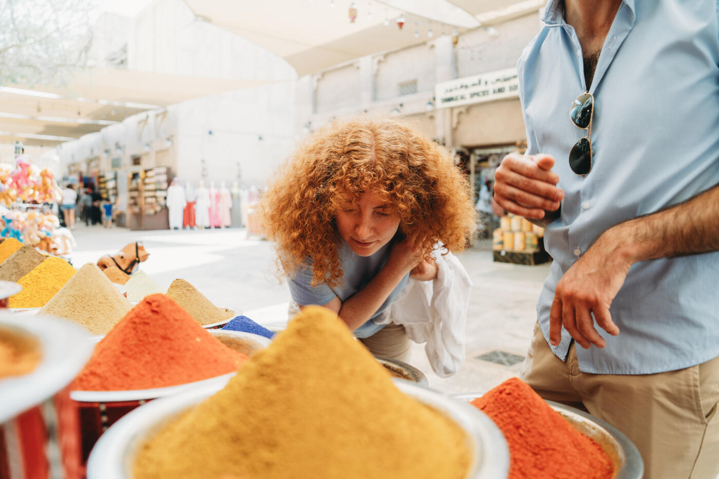 Young woman smelling colorful spices at Dubai Spice Souk in Old Dubai, United Arab Emirates, with her partner