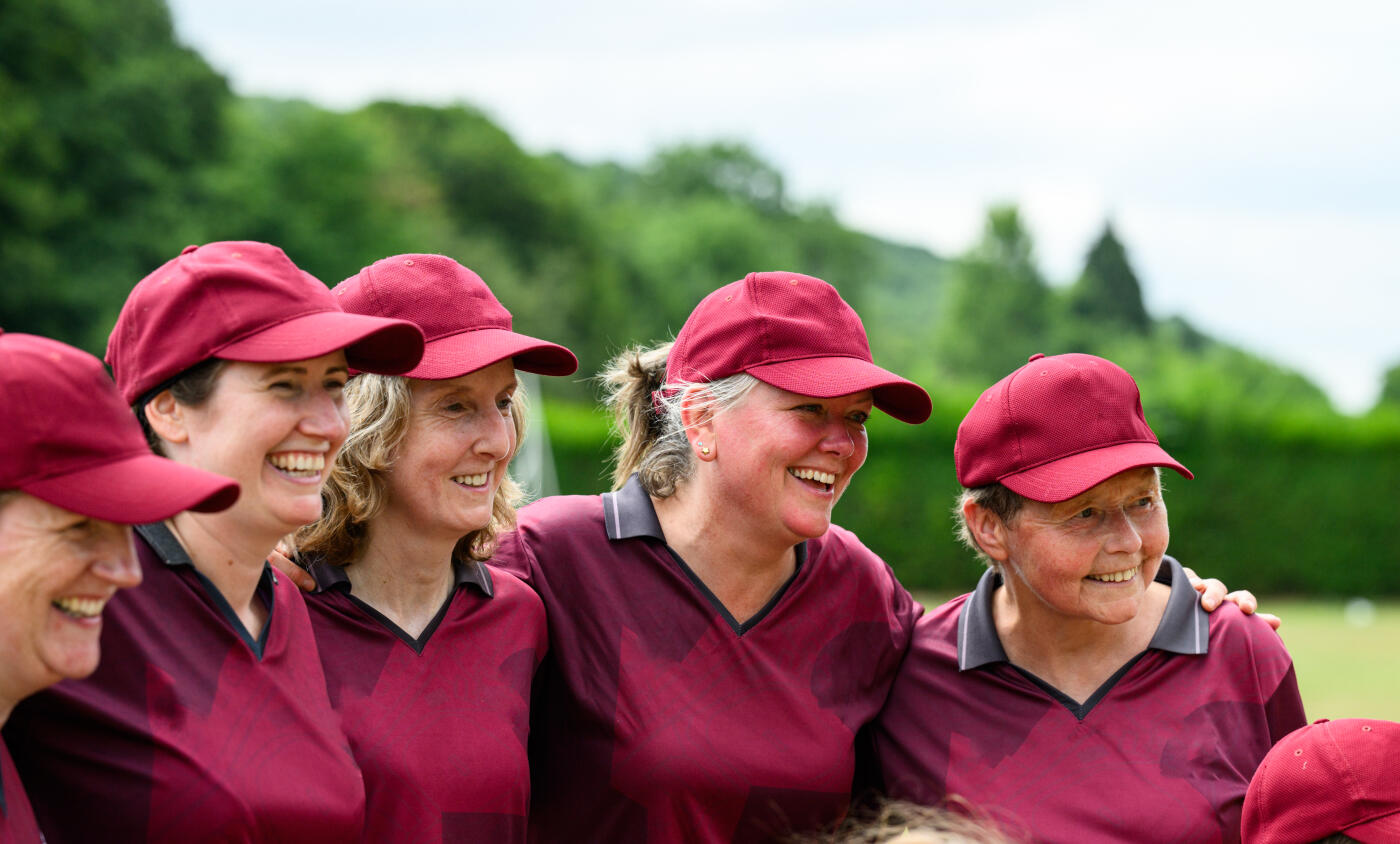 Women and Girls cricket teams playing a match on a sunny day outdoors on grass pitch