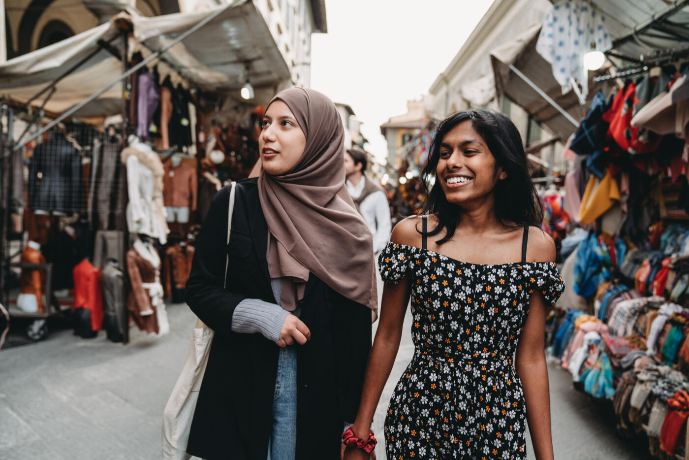 Two friends are walking in San Lorenzo market in Florence, Italy. They are shopping together.