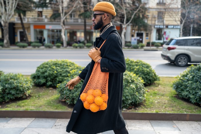 African American walking city street carrying oranges in reusable cotton mesh shopping bag