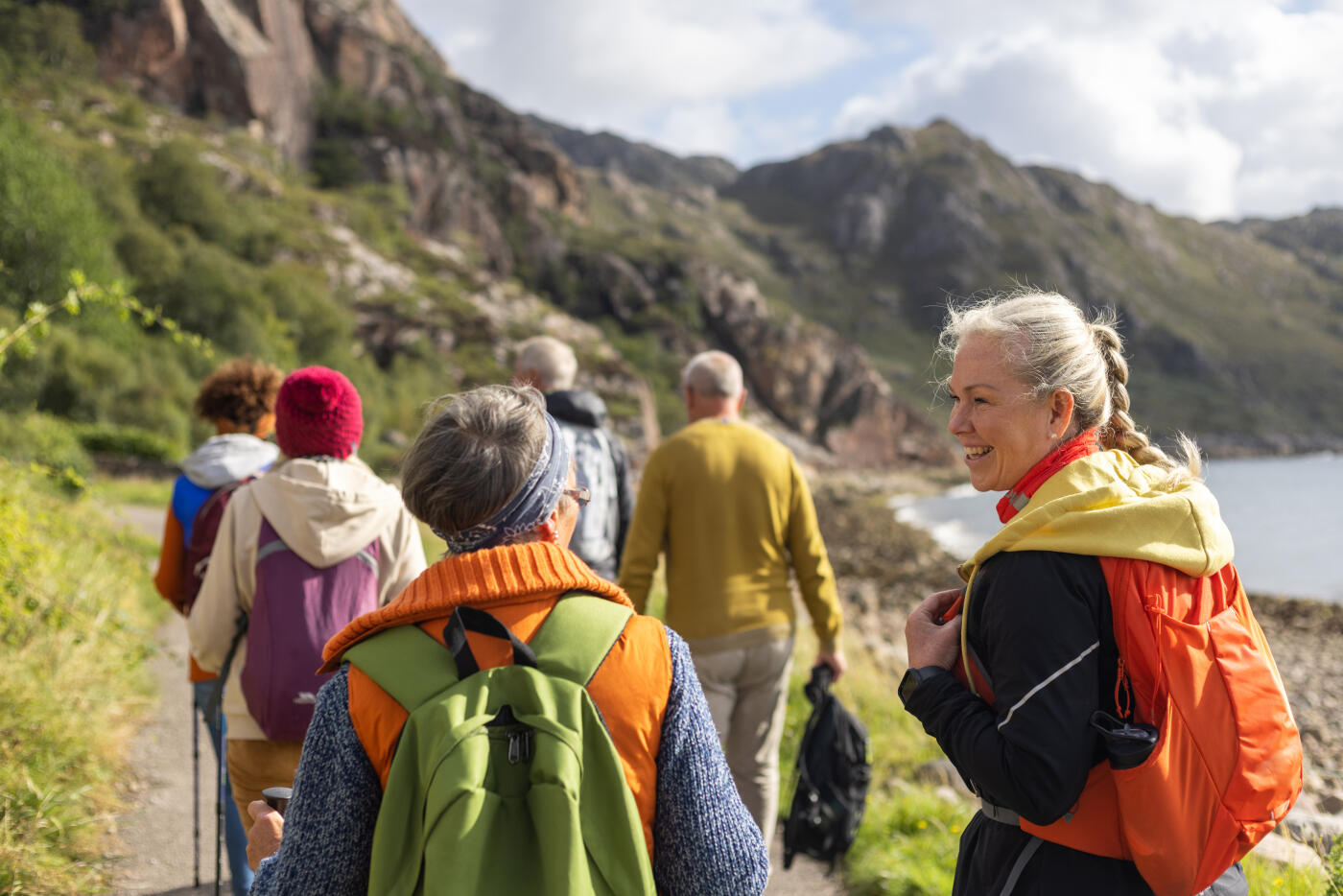 Waist-up rear view shot of a group of mature and senior friends walking along a footpath near the village of Diabaig on the side of Loch Torridon in the west highlands of Scotland. They are all talking to each other wearing vibrant walking clothing.