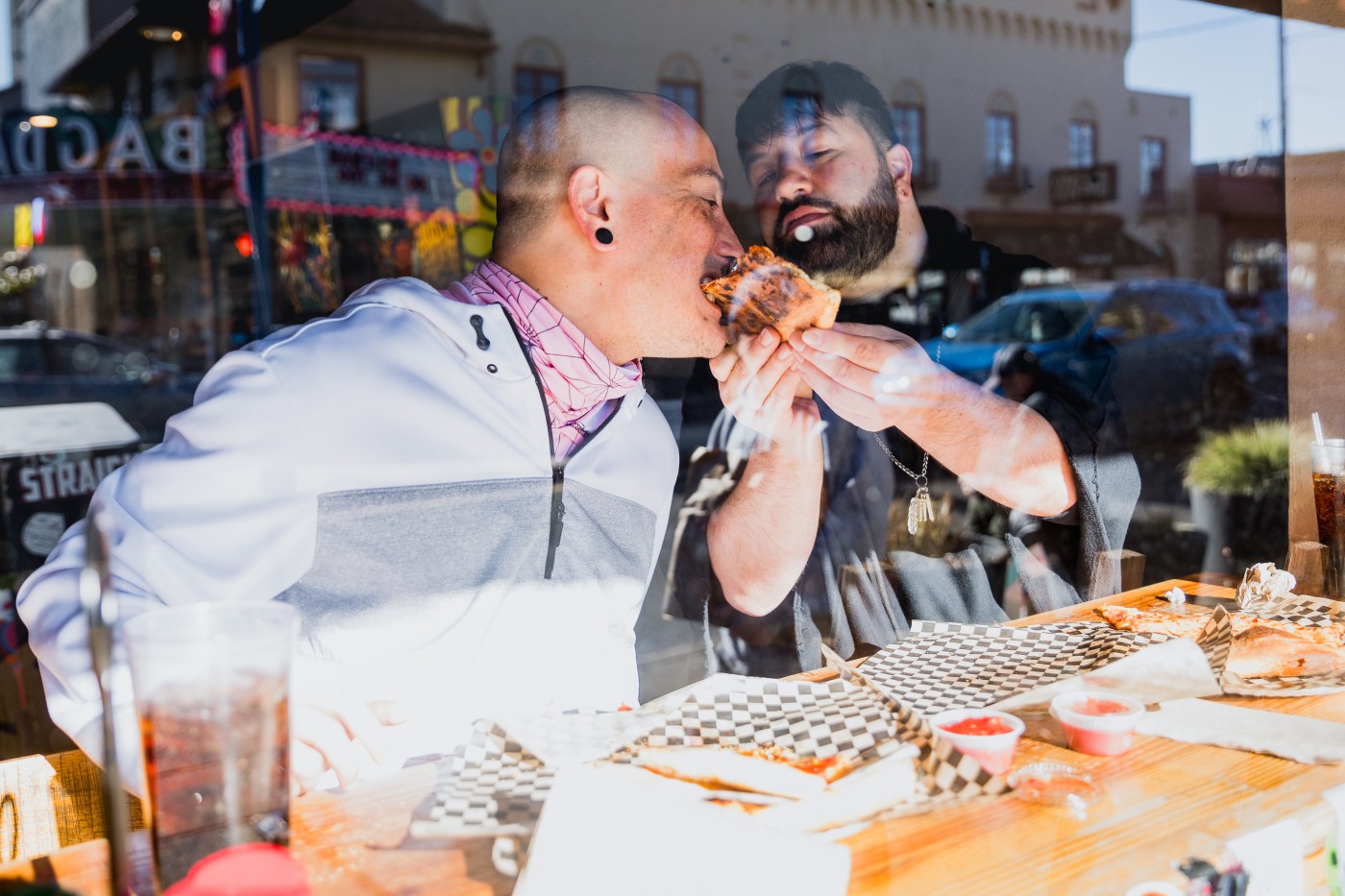A gay couple eating out at a restaurant. They are connecting with each other over the table as they enjoy their food from a corner pizza shop in the heart of Portland Oregon