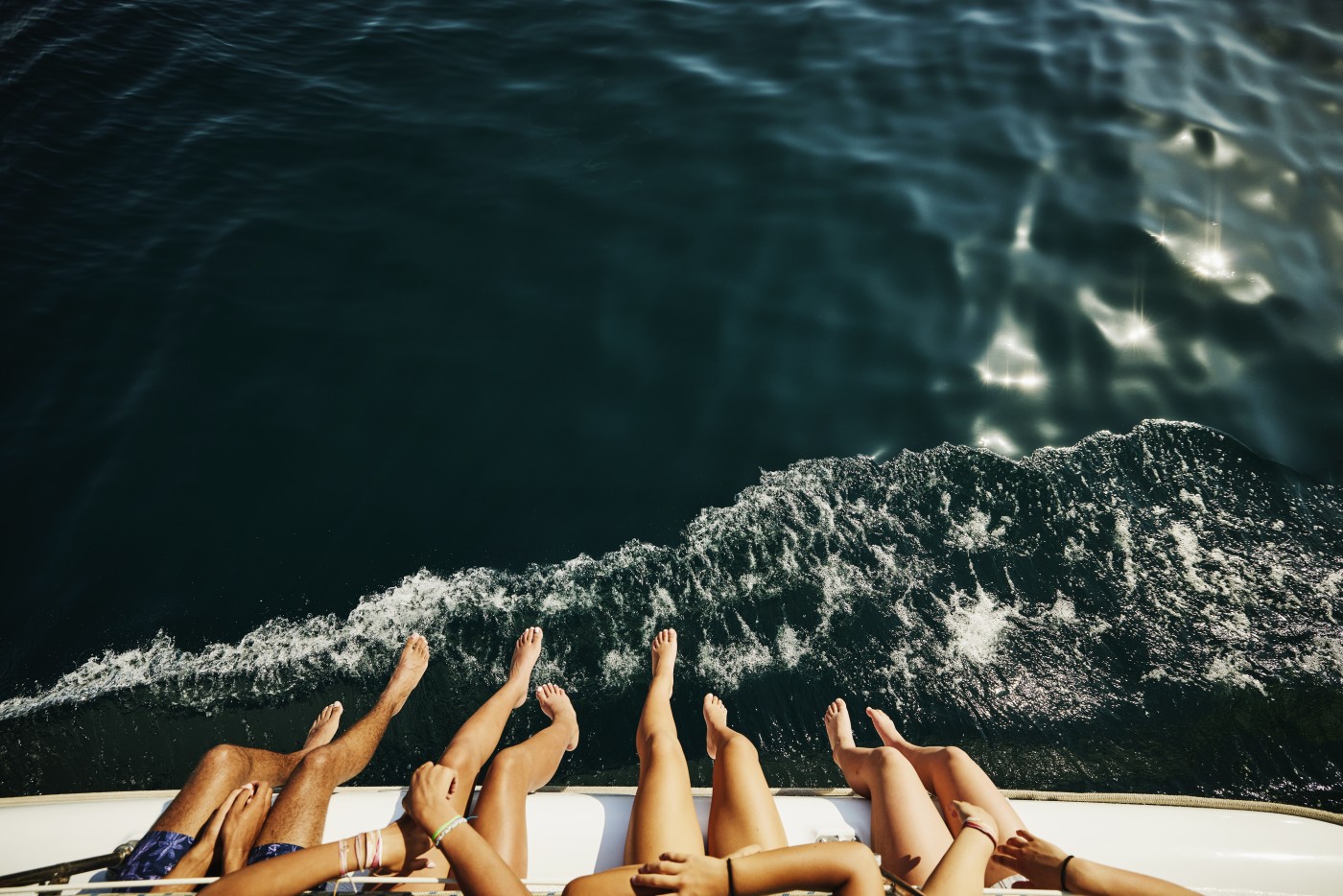 Medium shot overhead view of teenagers feet hanging over side of sailboat while on cruise during family vacation