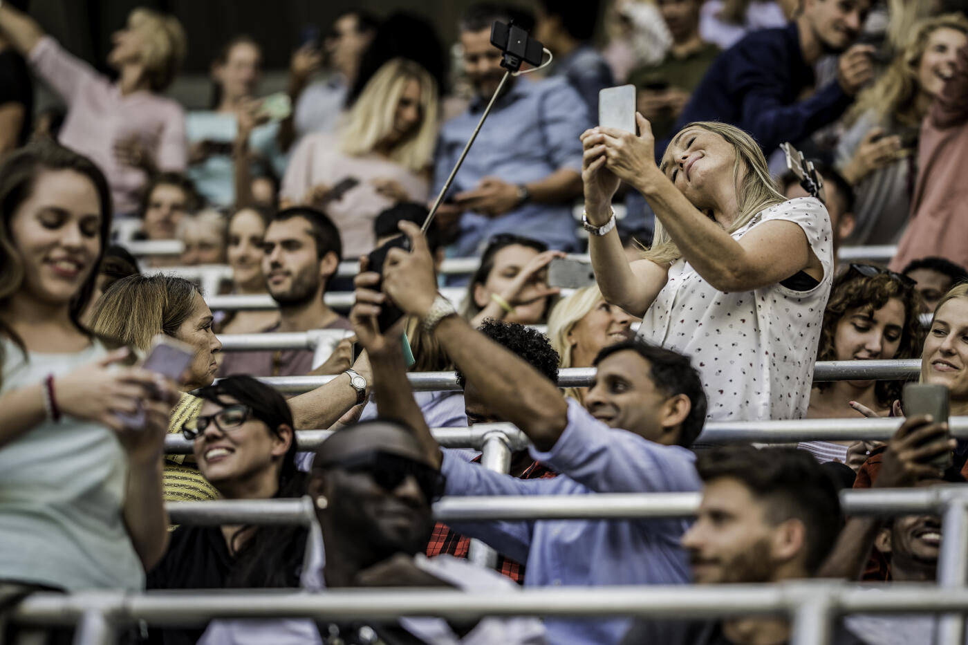 Large group of people posing for selfies while in a stadium crowd.
