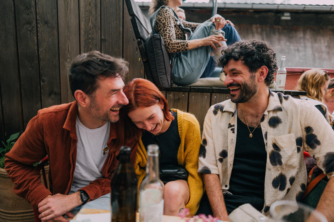Three friends enjoy a cheerful moment together at an outdoor social gathering. The atmosphere is lively, exemplifying happiness and connection among good company in a casual setting. Part of a series with video