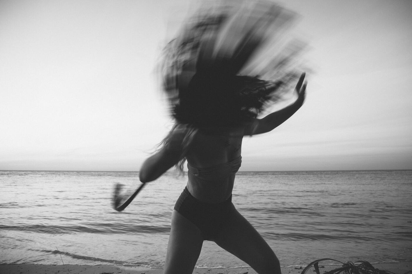 Blurry monochrome photo of girl dancing with a palm leaf on a beach