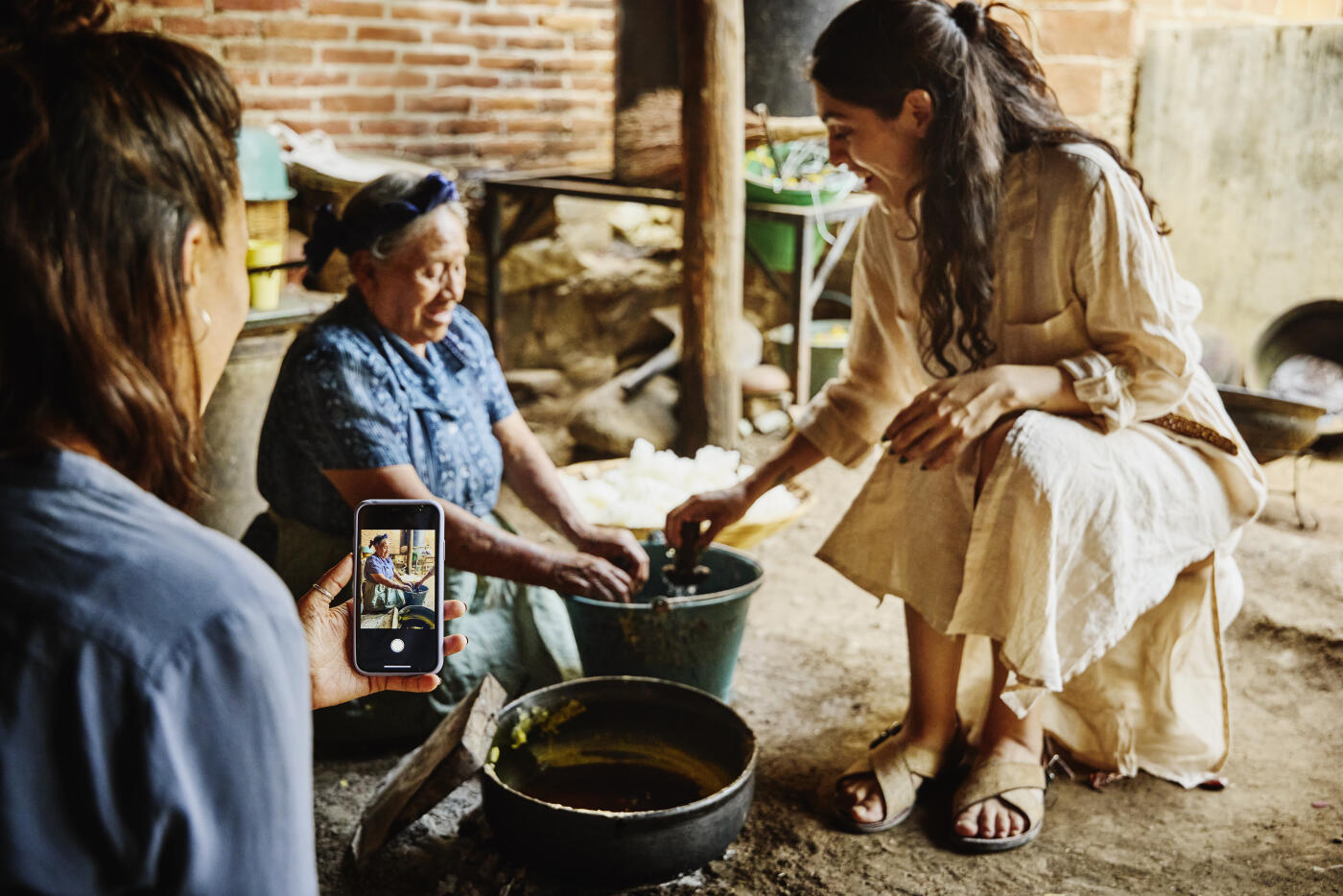 Medium wide shot of female tourist photographing her friend candlemaking with smartphone during Oaxacan crafts tour