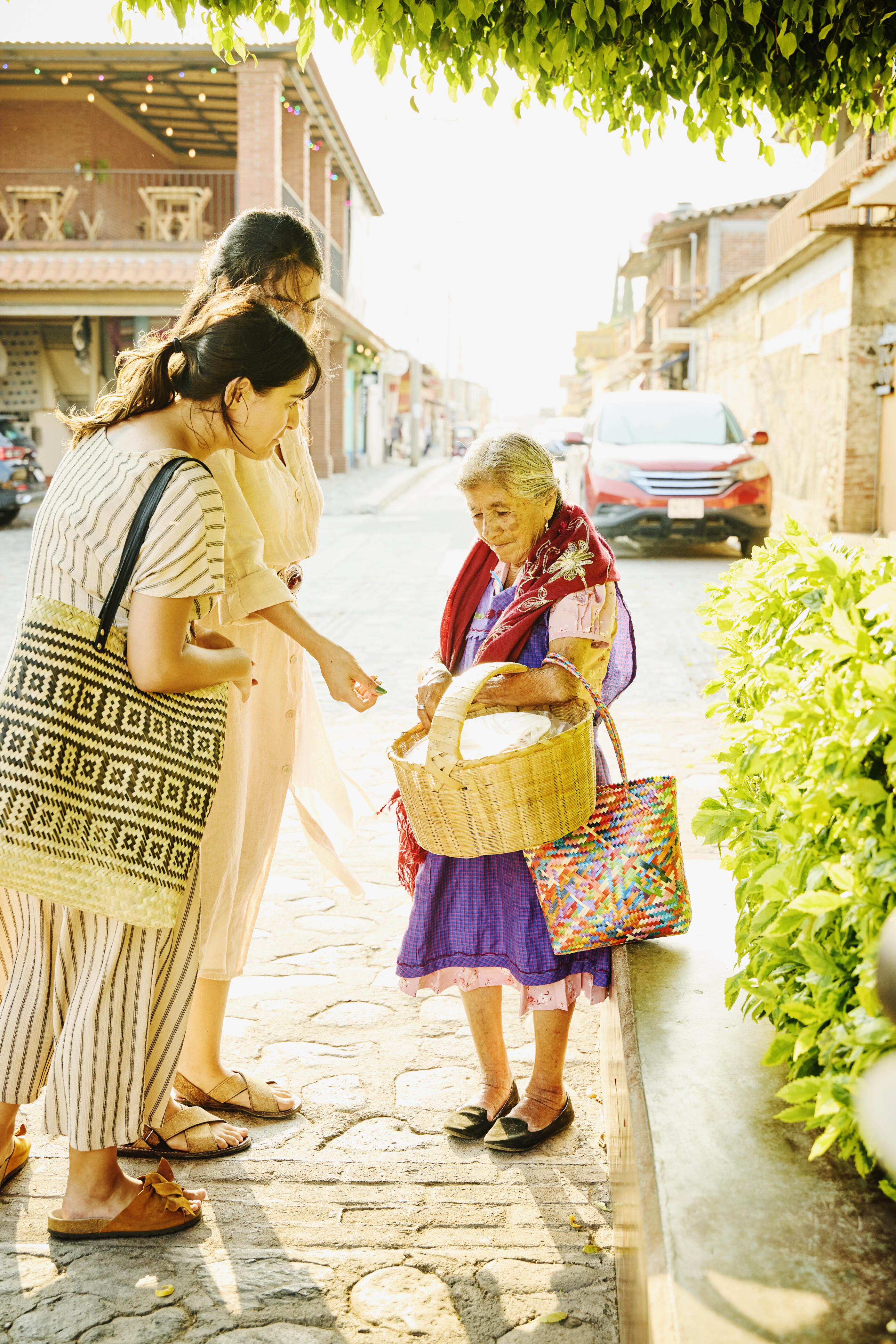 Wide shot of a female friends purchasing traditional Oaxacan snacks that are handmade by a local street food seller in a provincial town