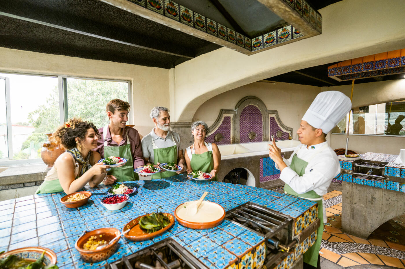 Chef takes a photo of a group of tourists holding plates with Chiles en Nogada that they cooked during class